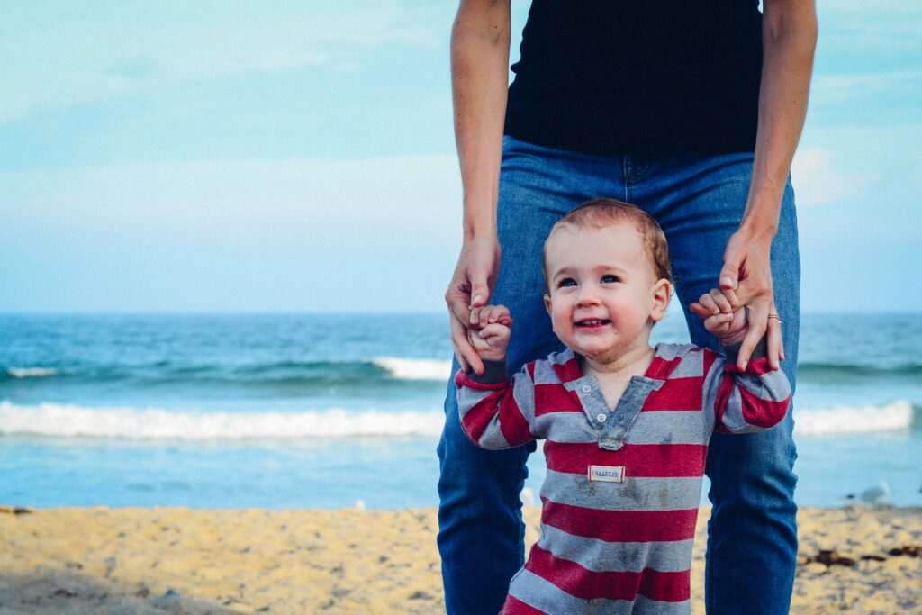 Smiling toddler holding hands while walking on the beach, enjoying a day by the ocean.