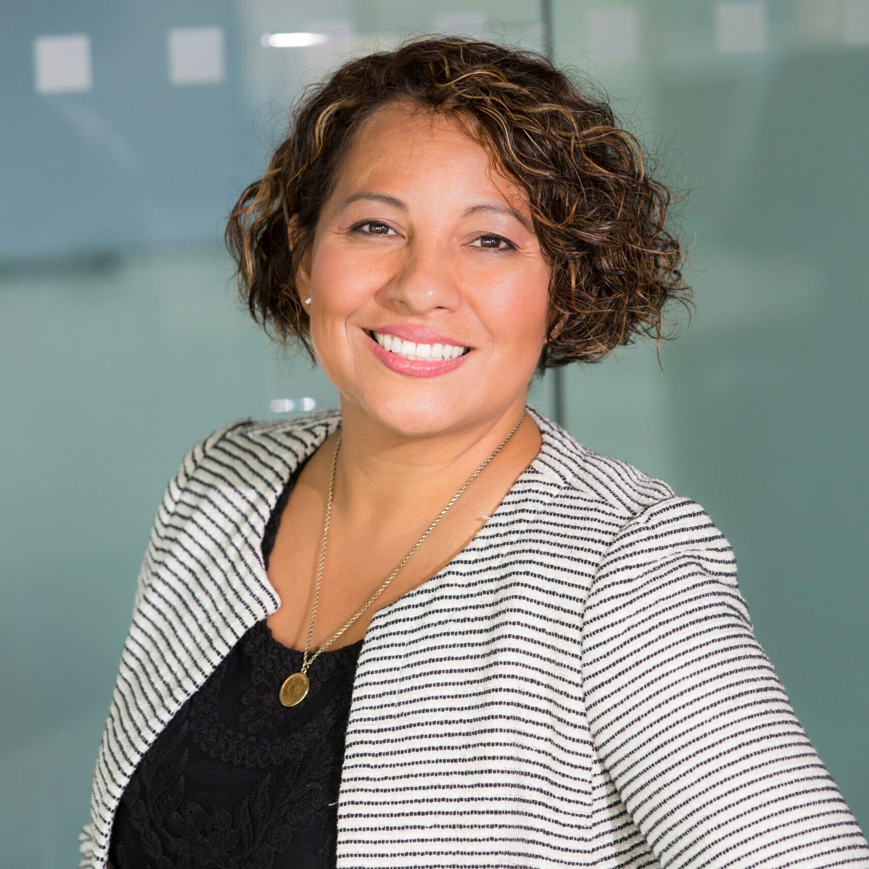 A professional woman smiling confidently while wearing a striped jacket in an office setting